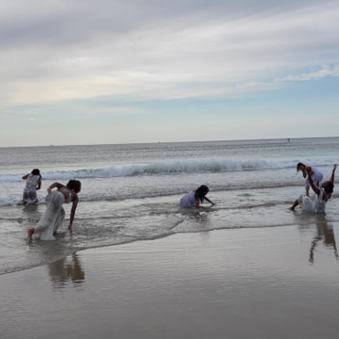 dancers, dressed in white, appear to be emerging from the ocean. 