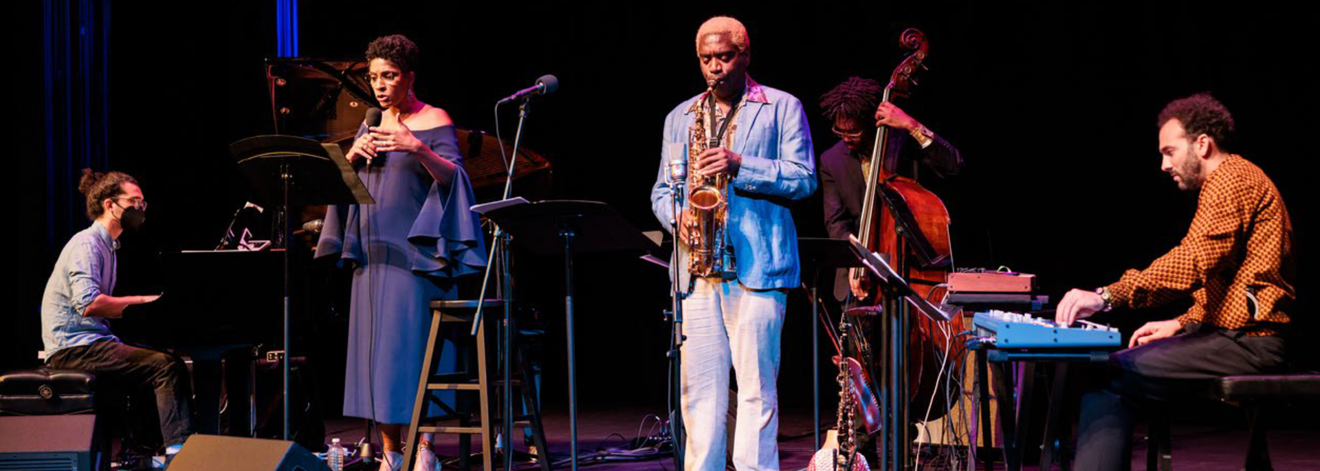 A singer, saxophonist, a bass player, and two keyboardists performing
